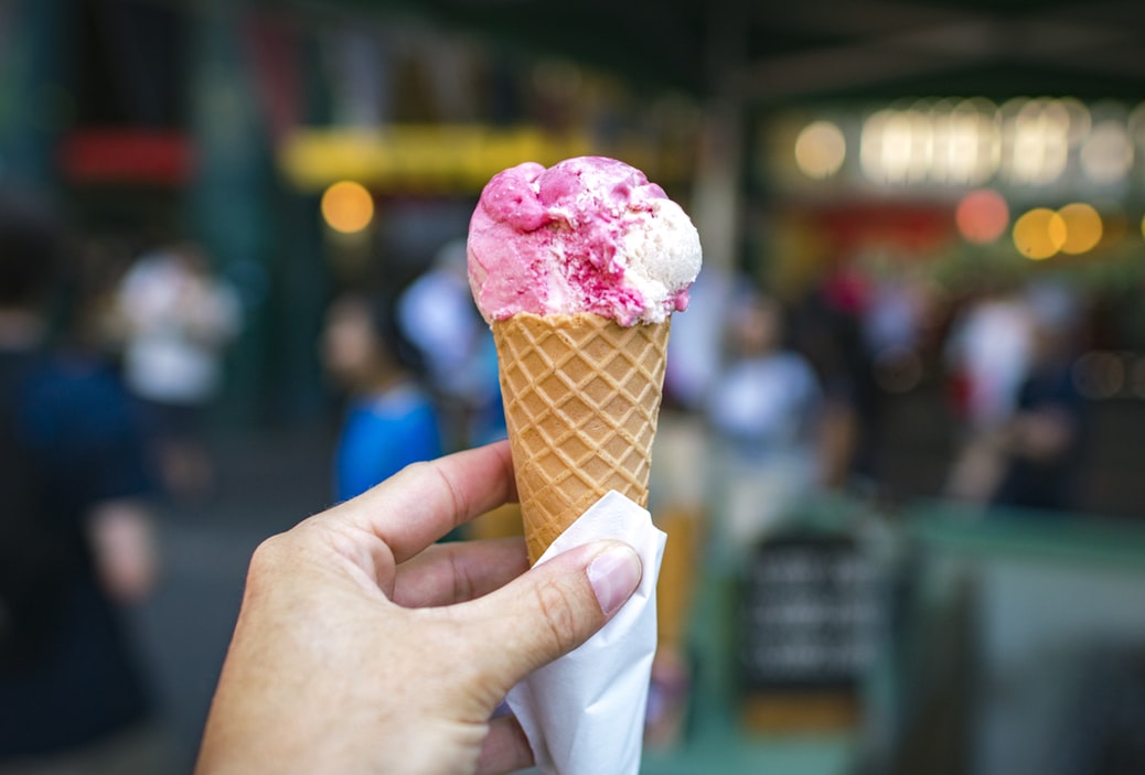 A person holding up a pink and white ice cream cone.